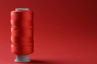 Kırmızı arkaplanda renkli dikiş ipliği makarası, metin için boşluk