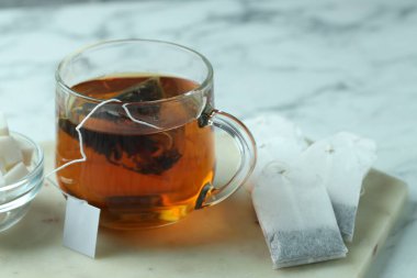 Cam bardakta çay poşeti, sıcak içecek ve şeker küpleri ışık masasında, yakın plan.