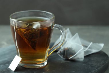 Cam bardakta çay poşeti, gri masada sıcak içecek, yakın plan.