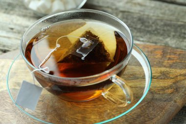 Cam bardakta çay poşeti, ahşap masada sıcak içecek, yakın plan.