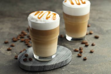 Bardakta latte macchiato ve gri masada kahve çekirdekleri, yakın plan.