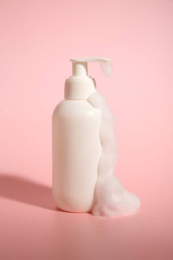 Pembe arka planda köpüklü bir şişe kozmetik ürünü.