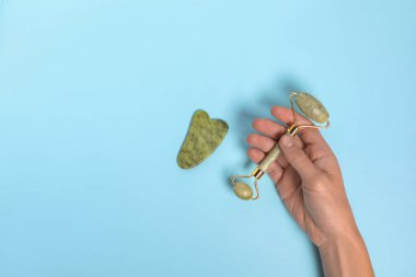 Yüz silindiri ve açık mavi arka planda gua sha aleti olan bir kadın. Metin için boşluk