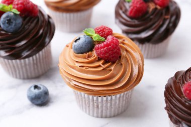 Çikolata kremalı ve böğürtlenli lezzetli kekler beyaz mermer masada, yakın plan.