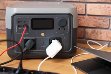 İçerideki ahşap masada taşınabilir elektrik santralinden dizüstü bilgisayar şarj ediliyor.