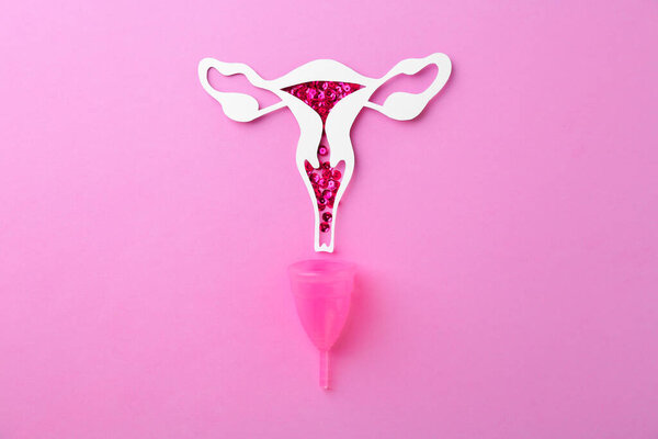 Paper uterus with sequins and menstrual cup on violet background, top view
