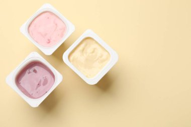 Sarı arka planda plastik bardaklarda lezzetli yoğurtlar. Metin için boşluk