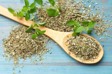 Kaşıkla kurutulmuş kekik ve açık mavi ahşap masada yeşil yapraklar, yakın plan.