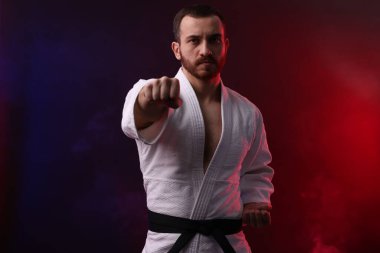 Üniformalı bir adam renkli ışıklarla ve dumanla karate yapıyor.