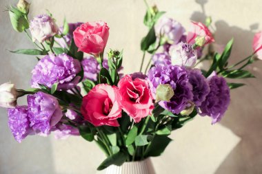 Bej duvarın yanında güzel Eustoma çiçekleri olan vazo, yakın plan.