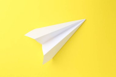 Sarı arka planda bir el yapımı kağıt uçak, üst görünüm.