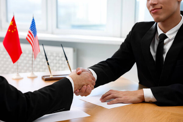 Diplomats shaking hands during meeting at wooden table indoors, closeup