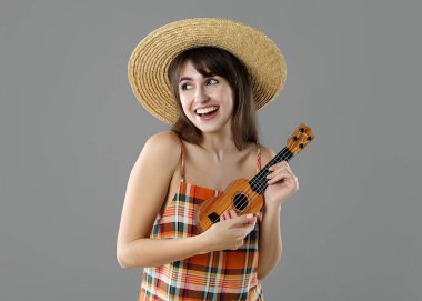 Gri arka planda ukulele çalan mutlu kadın