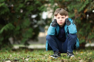 Autism concept. Lonely little boy covering his ears outdoors, space for text clipart