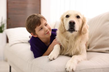 Evdeki kanepede sevimli köpeğiyle oturan çocuk.