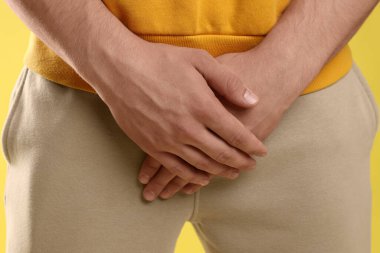 Cinsel yolla bulaşan hastalıklar. Sarı arka planda belirtilerden muzdarip bir adam, yakın plan.