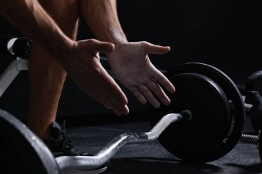 Spor salonunda halterle eğitilmeden önce talk pudrasıyla el çırpan adam, yakın plan.