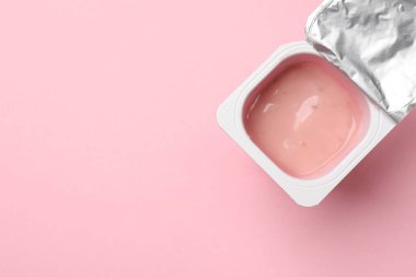 Açık pembe arka planda plastik bardakta lezzetli yoğurt, üst manzara. Metin için boşluk