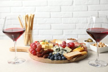 Farklı çeşitlerde lezzetli peynir, diğer atıştırmalıklar ve şarap açık gri masada.