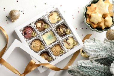 Mücevher şeklinde lezzetli çikolata şekerlemeleri ve beyaz arka planda Noel süsü dolu bir kutu.