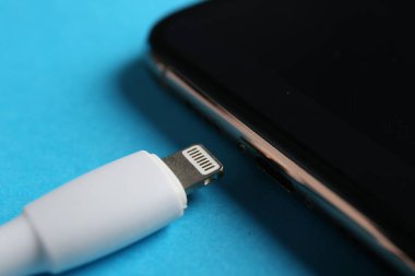 USB kablosu ışık konnektörü ve açık mavi arkaplanda akıllı telefon, yakın çekim