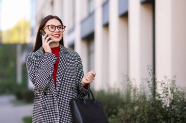 Şık takım elbiseli güzel bir kadın dışarıda akıllı telefondan konuşuyor. Metin için boşluk