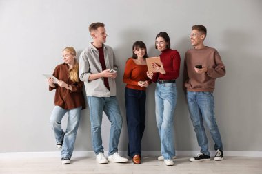 Açık gri duvarın yanında farklı aletler kullanan bir grup insan. Modern teknoloji