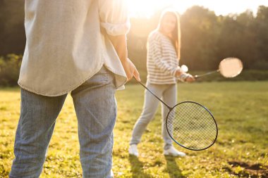 Güneşli bir günde parkta badminton oynayan genç bir kadın ve erkek.
