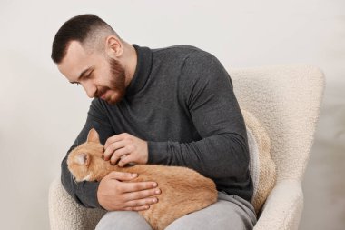 Evdeki koltukta sevimli kızıl kediyi okşayan adam.