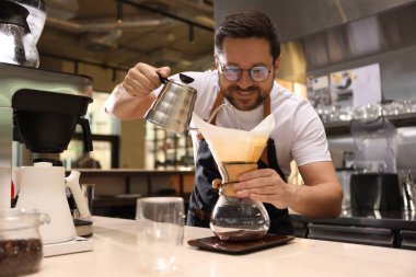 Barista kahve makinesinde kahve yapıyor. Kafedeki masada kağıt filtresi var.