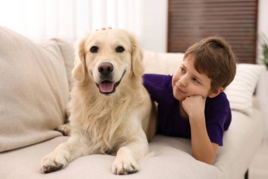 Evdeki kanepede sevimli köpeğiyle oturan çocuk.