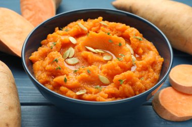 Tatlı patates püresi ve kabak tohumları kasede ve taze sebzeler mavi ahşap masada, yakın plan.