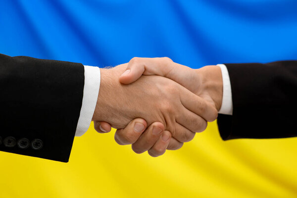 Diplomats shaking hands against flag of Ukraine, closeup