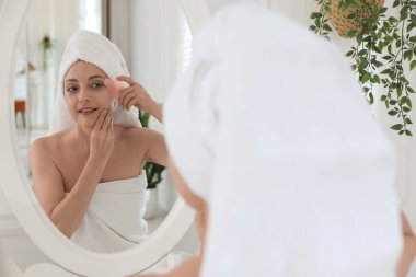 Gülümseyen kadın tuvaletteki aynanın yanında gua sha aletiyle yüz masajı yapıyor.