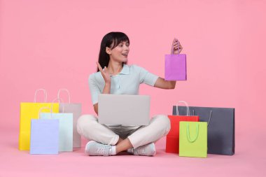 İnternet alışverişi. Dizüstü bilgisayarı ve pembe arka planda renkli çantaları olan mutlu kadın.