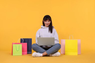 İnternet alışverişi. Laptoplu ve turuncu çantalı mutlu kadın.