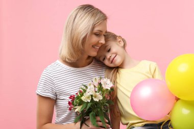 Küçük kızı pembe arka planda bir buket alstromerya çiçeği ve balonlarla annesini tebrik ediyor. Anneler Günün kutlu olsun.