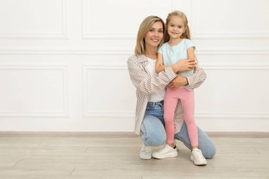 Mutlu anne ve tatlı kızı beyaz duvarın yanında.