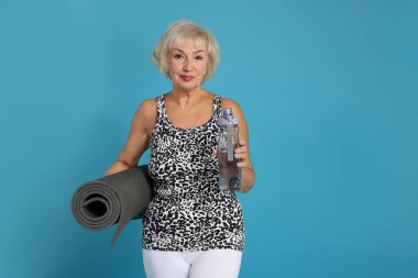 fitness paspası ve açık mavi arka planda suyu olan son sınıf kadın, metin için yer var.
