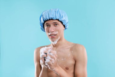 Duş bonesi ve açık mavi arka planda ağ süngeri olan bir adam.