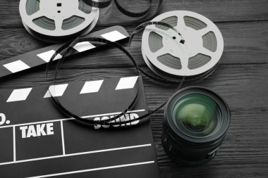 Film alkışı, film makaraları ve kamera lensleri siyah ahşap masanın üstünde.