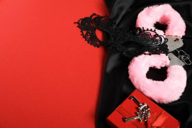 Pembe tüylü kelepçeler, dantel maske, anahtarlar ve kırmızı arka planda siyah kumaş, metin için boşluk