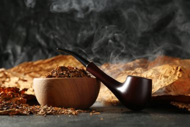 Tütün, kurumuş yapraklar ve siyah masada tüttüren pipo.