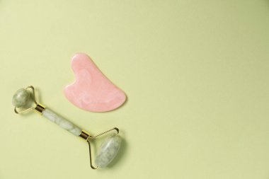 Açık yeşil arka planda yüz silindiri ve gua sha aracı, üst görünüm. Metin için boşluk