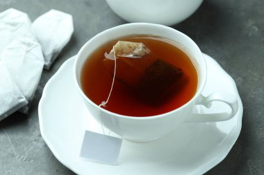 Çay poşetleri ve bardakla sıcak içecek gri desenli masada, yakın plan.