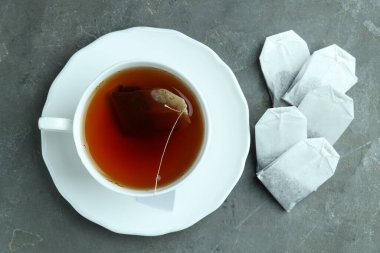 Çay poşetleri ve bardakta sıcak içecek gri desenli masa, düz uzanmış