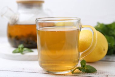 Limonlu aromatik nane çayı ve beyaz ahşap masa üzerinde taze yapraklar, yakın plan.