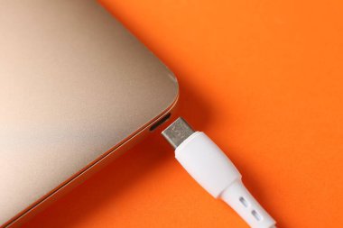 USB kabloyu turuncu arka planda dizüstü bilgisayarla şarj et, yakın plan. Metin için boşluk