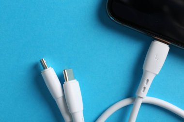 Açık mavi arkaplanda akıllı telefona bağlı USB şarj kablosu, üst görünüm