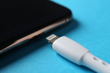 USB kablosu ışık konnektörü ve açık mavi arkaplanda akıllı telefon, yakın çekim